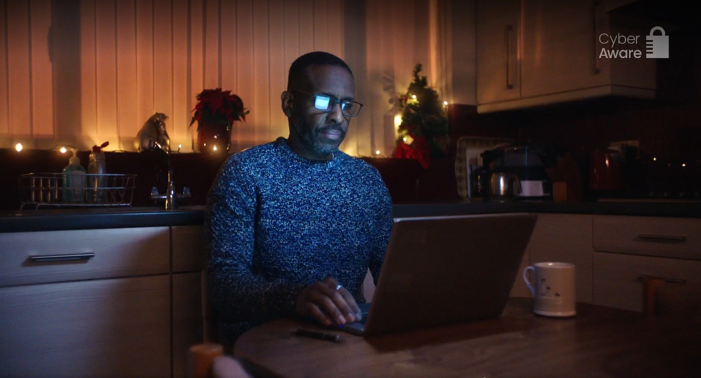 A frame from the Cyber Aware TV advert showing a man at a laptop in his kitchen