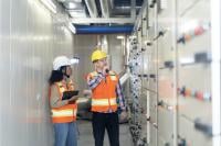 male and female in orange high vis vests and hard hats looking at an electrical unit