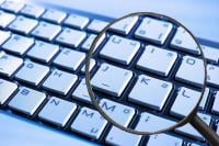 Image shows a white keyboard with keys on the right hand side of the board magnified through the lens of a magnifying glass
